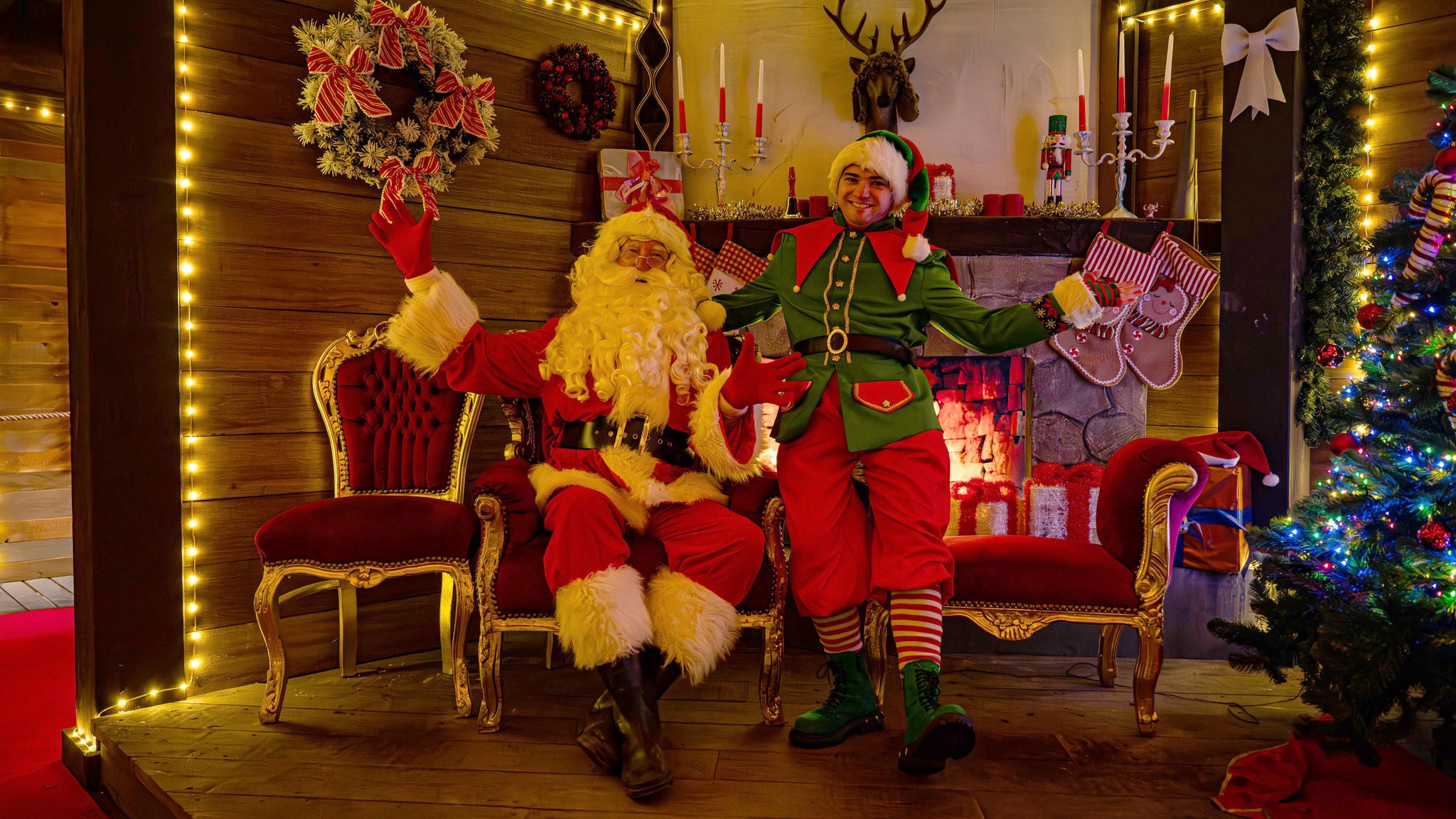 Kerstman en kerstelf zwaaien vanop een stoel voor de haard in het Huis van de Kerstman.