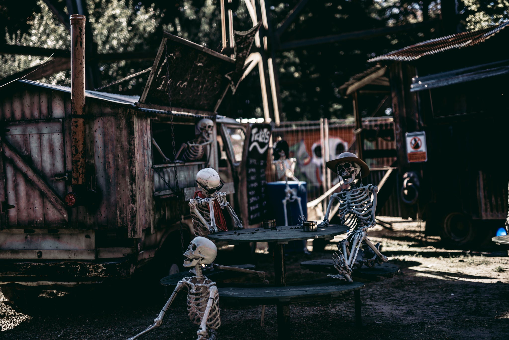 Skeletten zitten aan een picknick bank voor een foodtruck als halloweendecoratie.